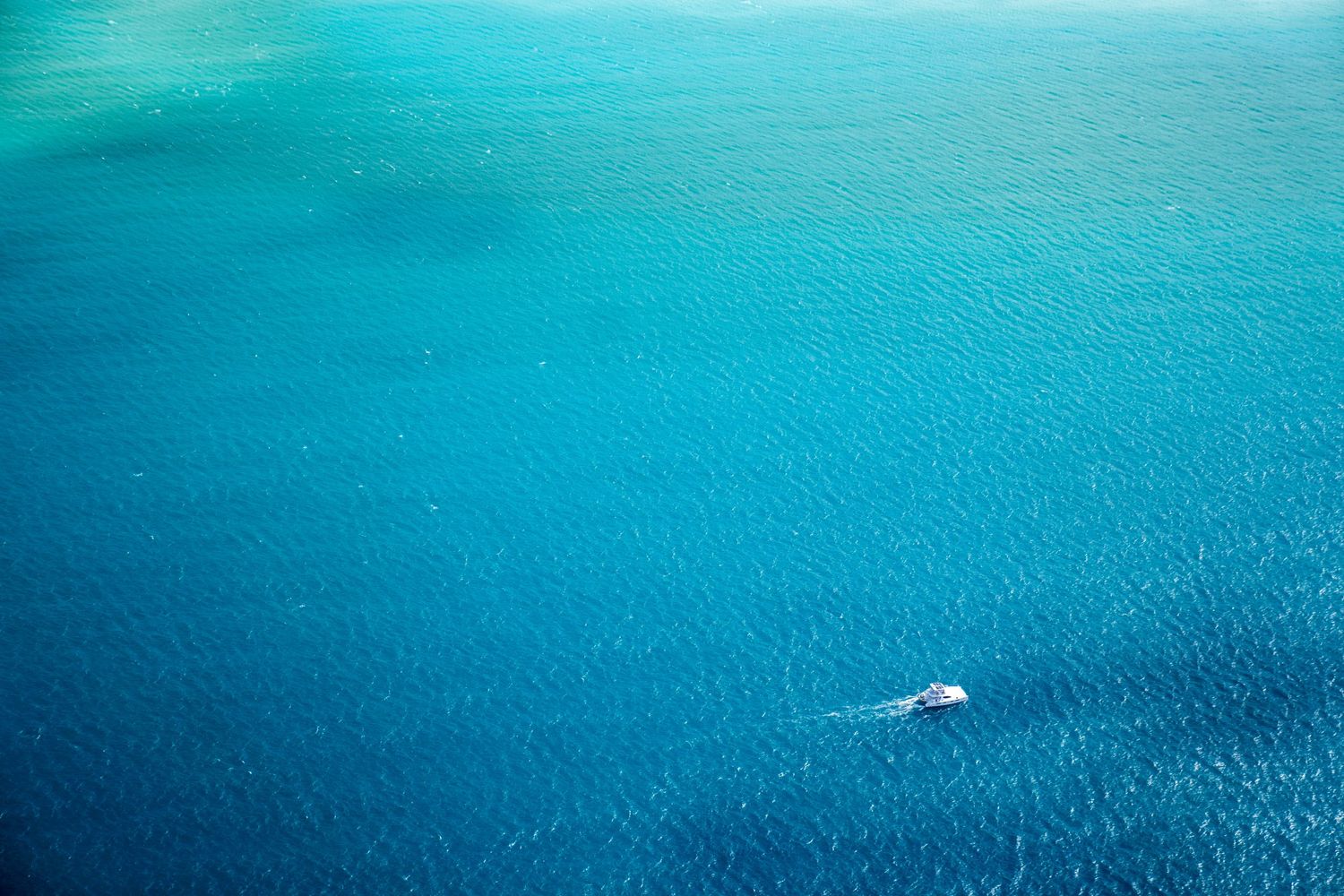 Single white boat cruising through vast expanse of deep blue ocean waters.