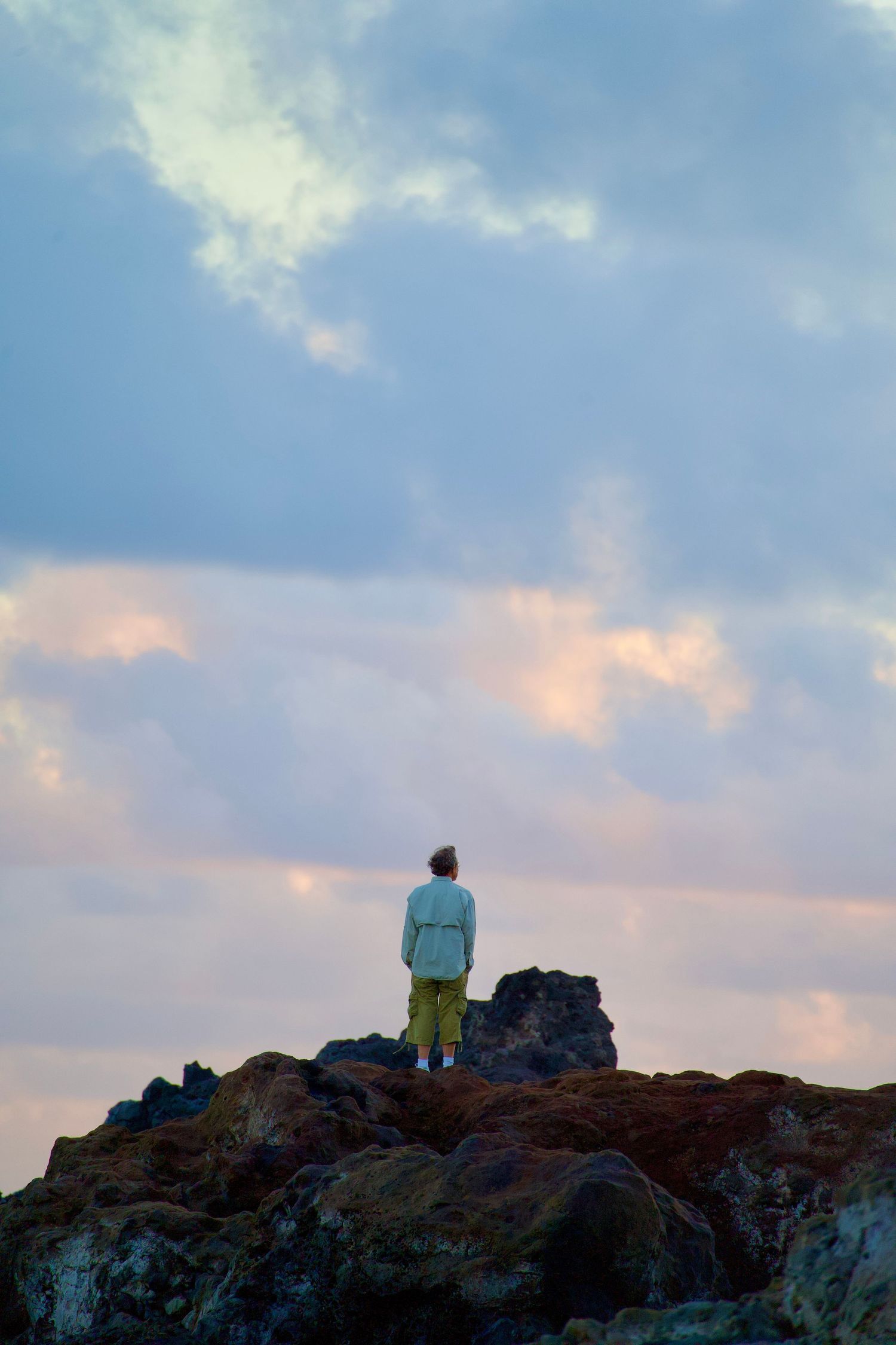 Silhouetted figure standing on rocky outcrop against colorful sunset sky.