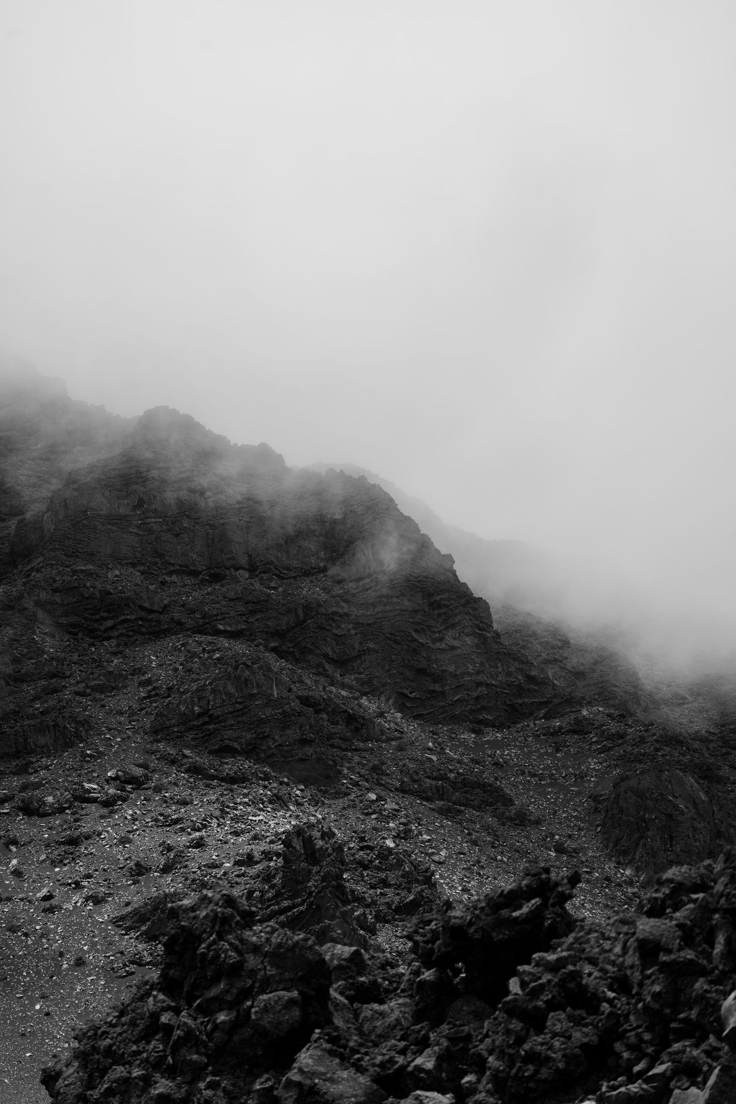 Moody black and white landscape of misty mountain cliffs and rocky terrain.