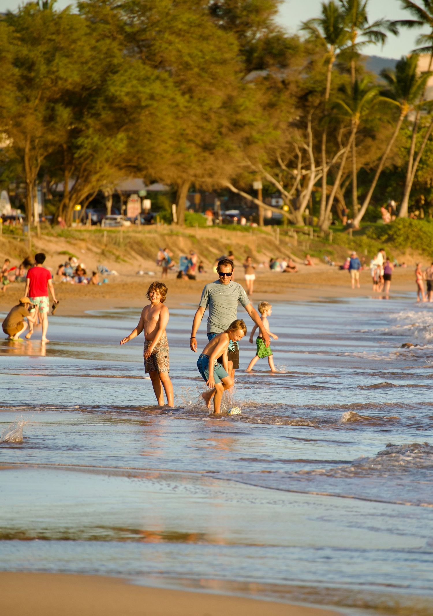 Beachgoers enjoying the shallow waves at a tropical beach during golden hour.