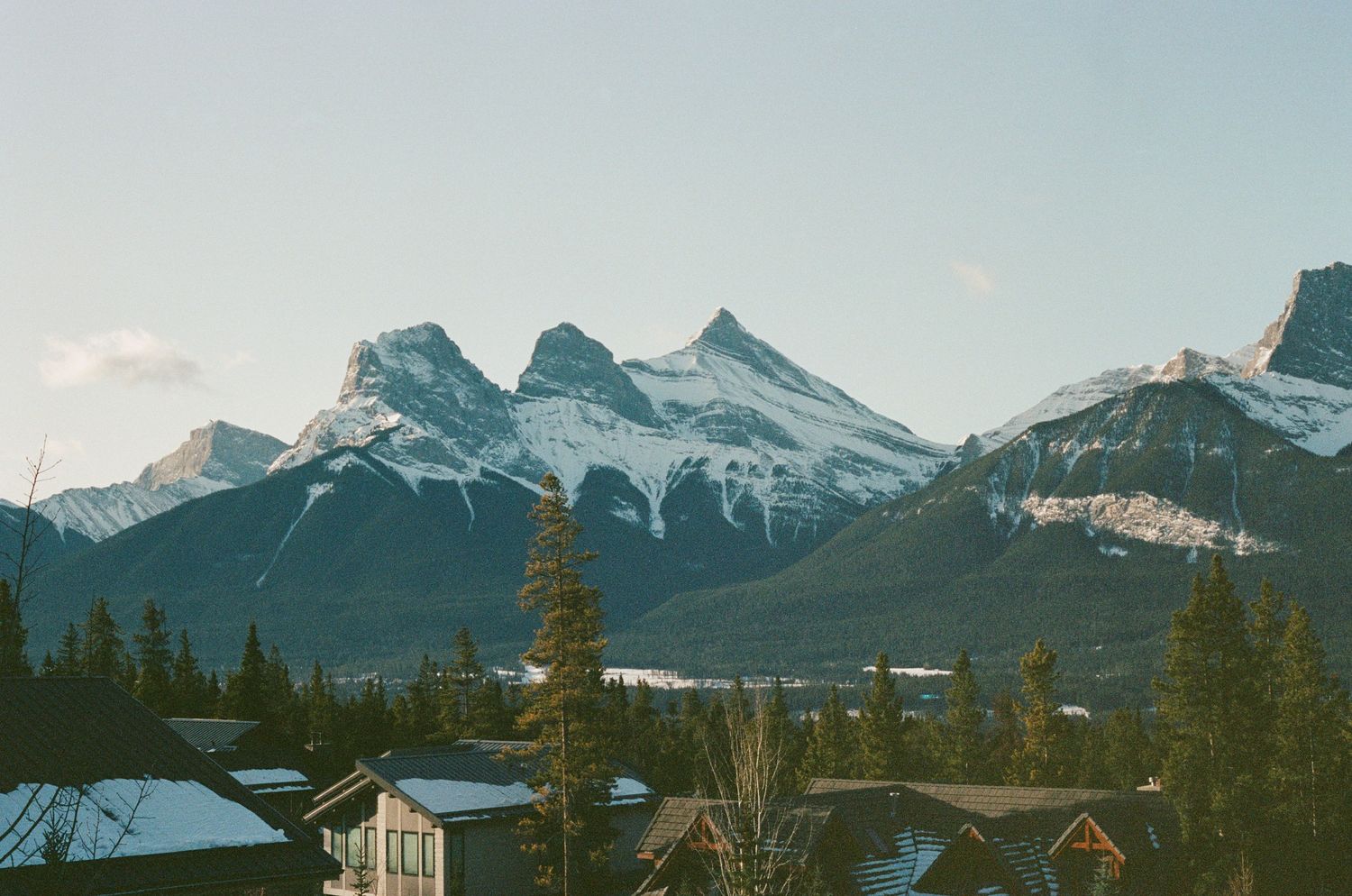 Snow-covered Canadian Rockies tower over small mountain town houses nestled below.