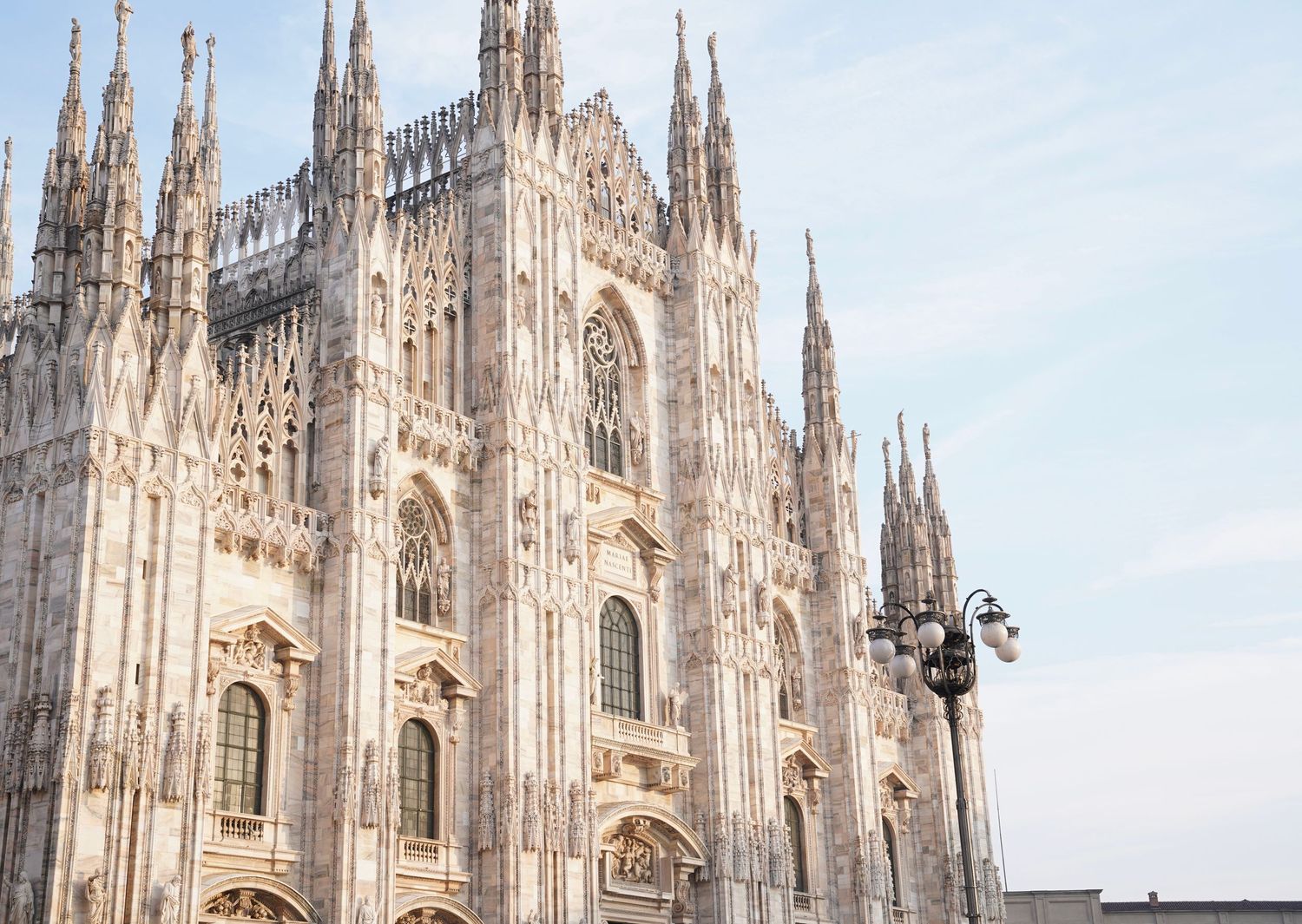 Gothic spires and ornate architecture of Milan Cathedral against clear sky.