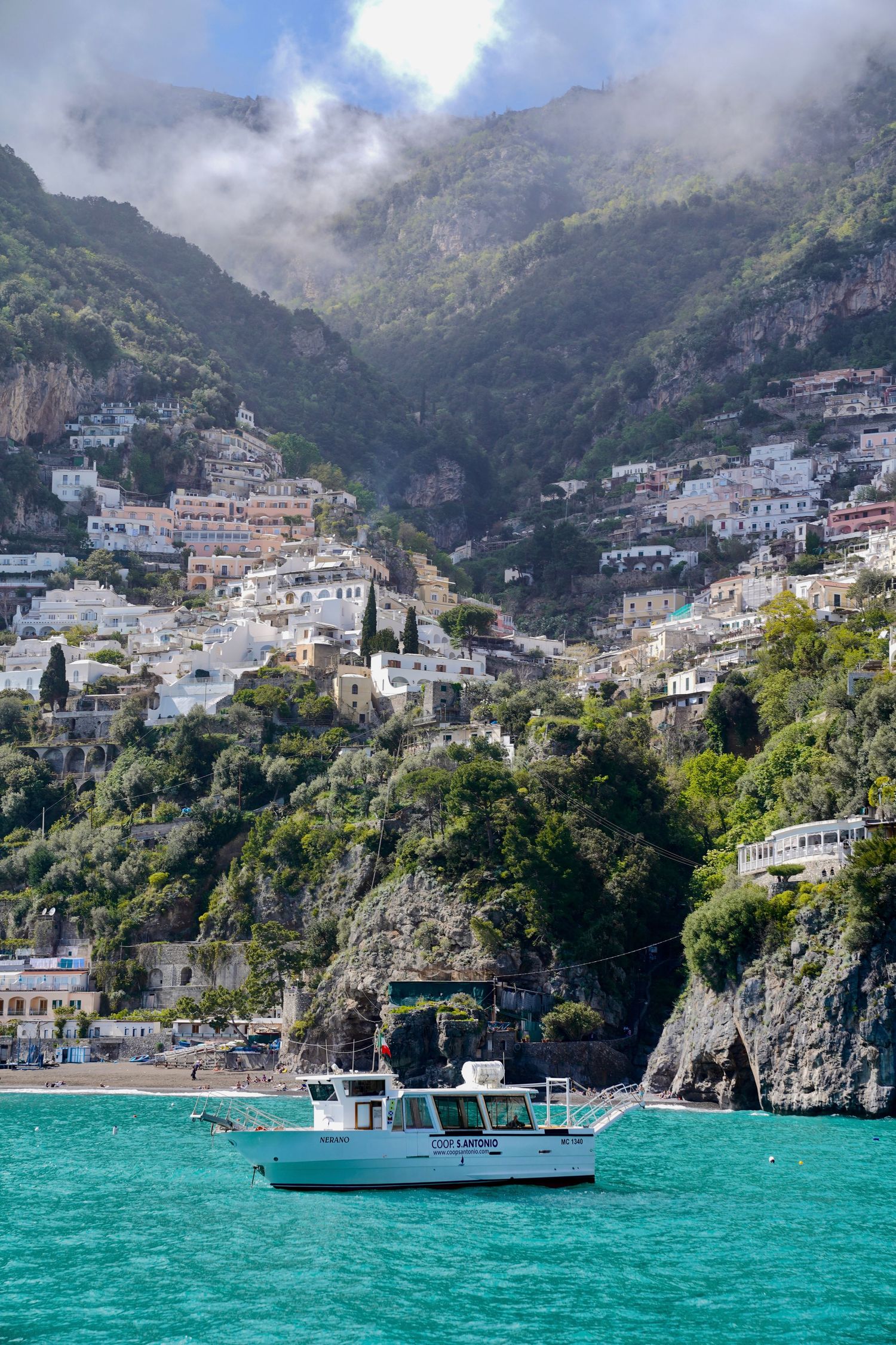Colorful coastal town nestled in mountains with turquoise water and boats in Positano, Italy.
