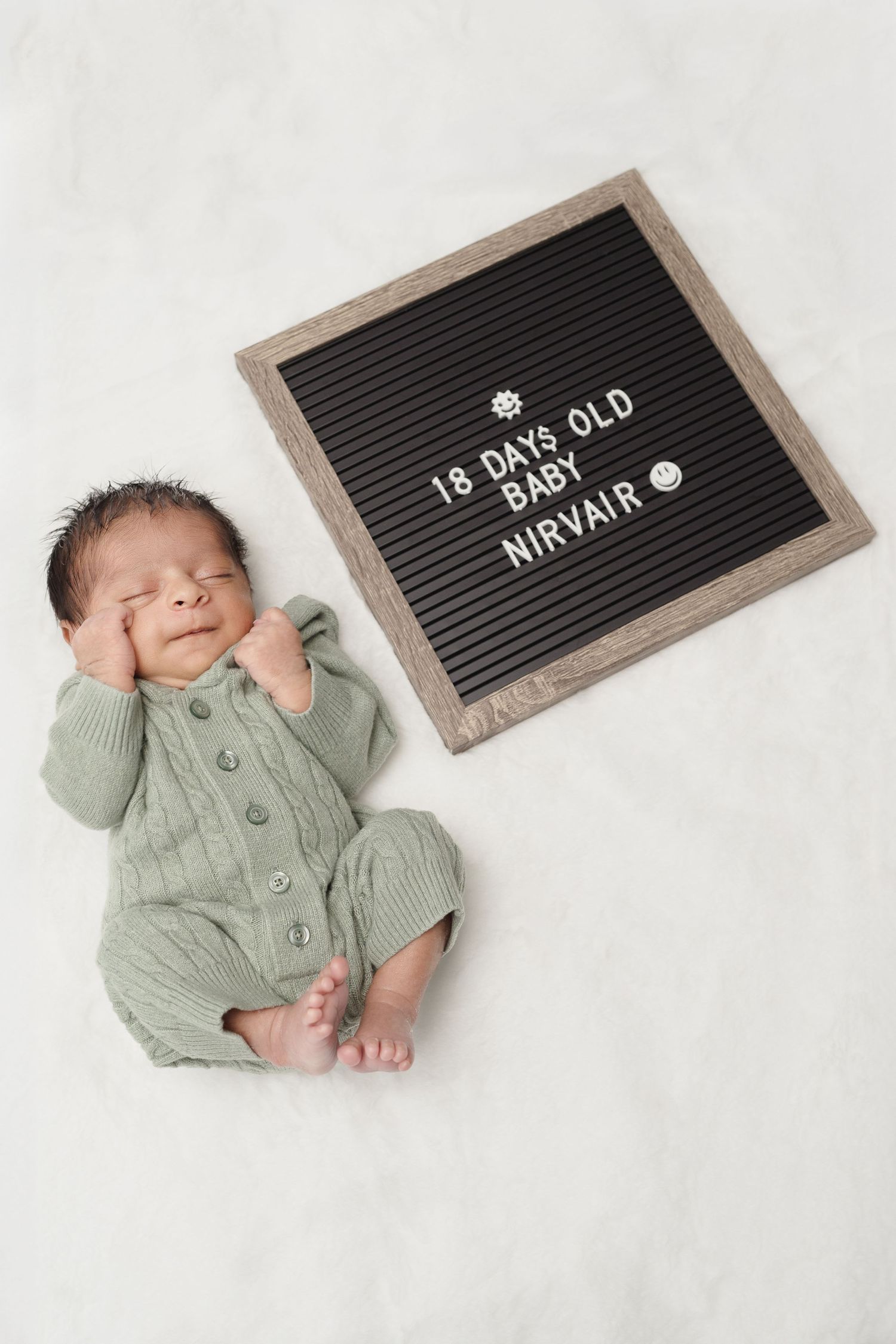 Newborn in sage green outfit next to letterboard announcing 18 days old.