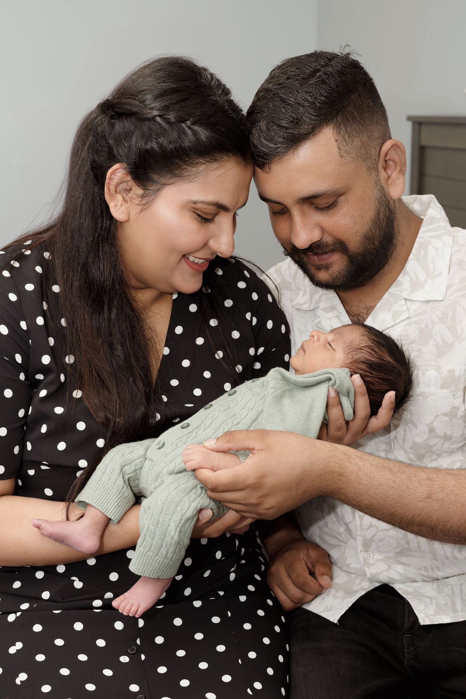 A tender family moment as parents cuddle their newborn wearing mint green on a couch.