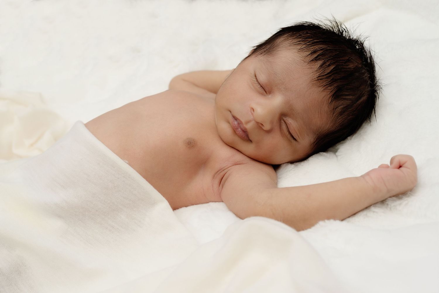 Sleeping newborn baby lying peacefully on white blanket.