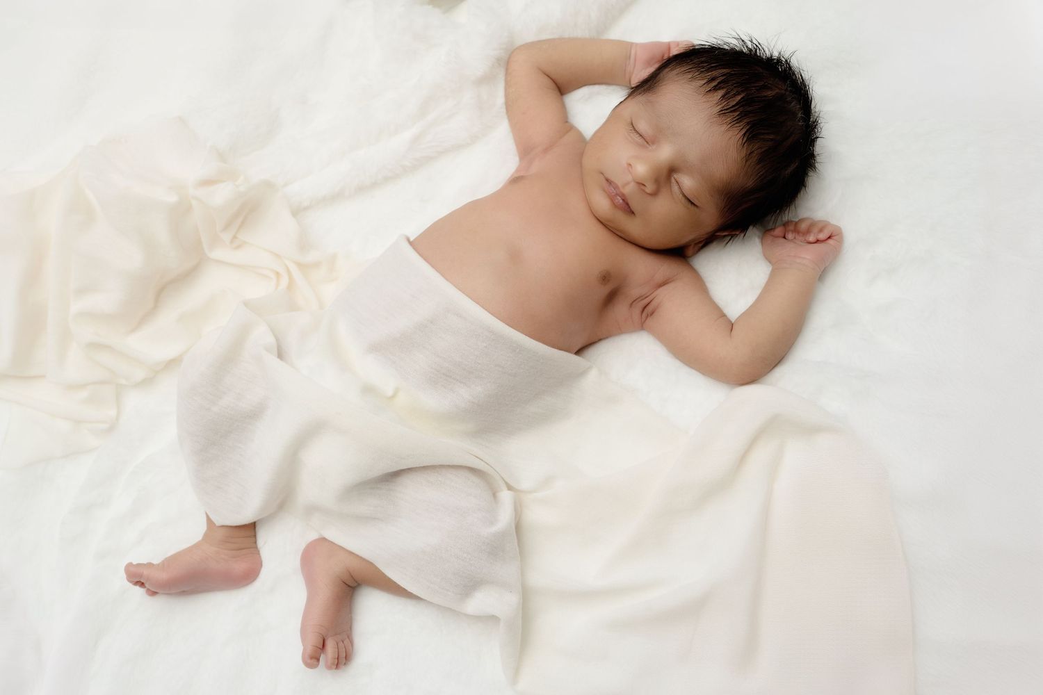 Peaceful sleeping newborn draped in soft white fabric.