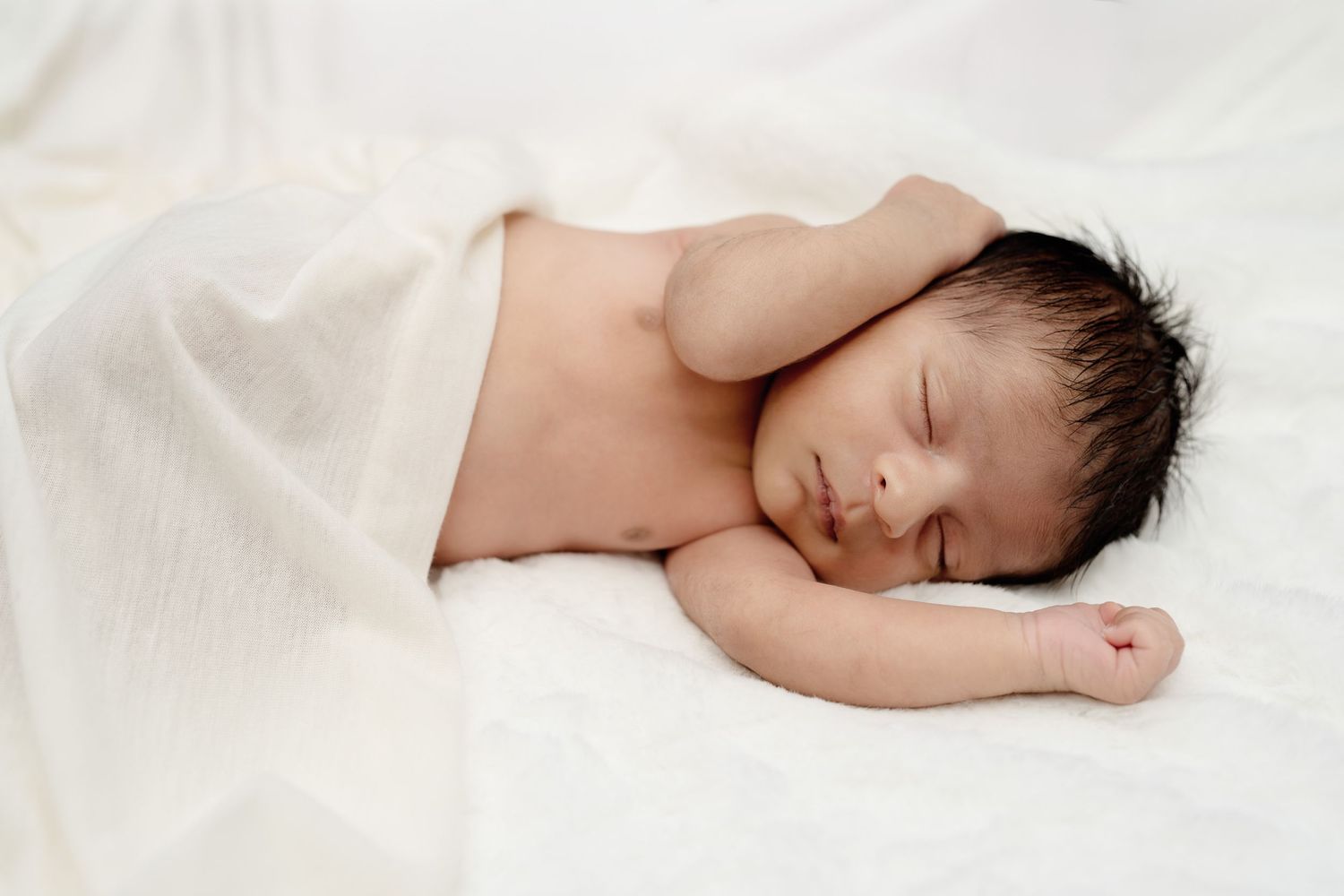 Sleeping baby wrapped in white blanket against white background.