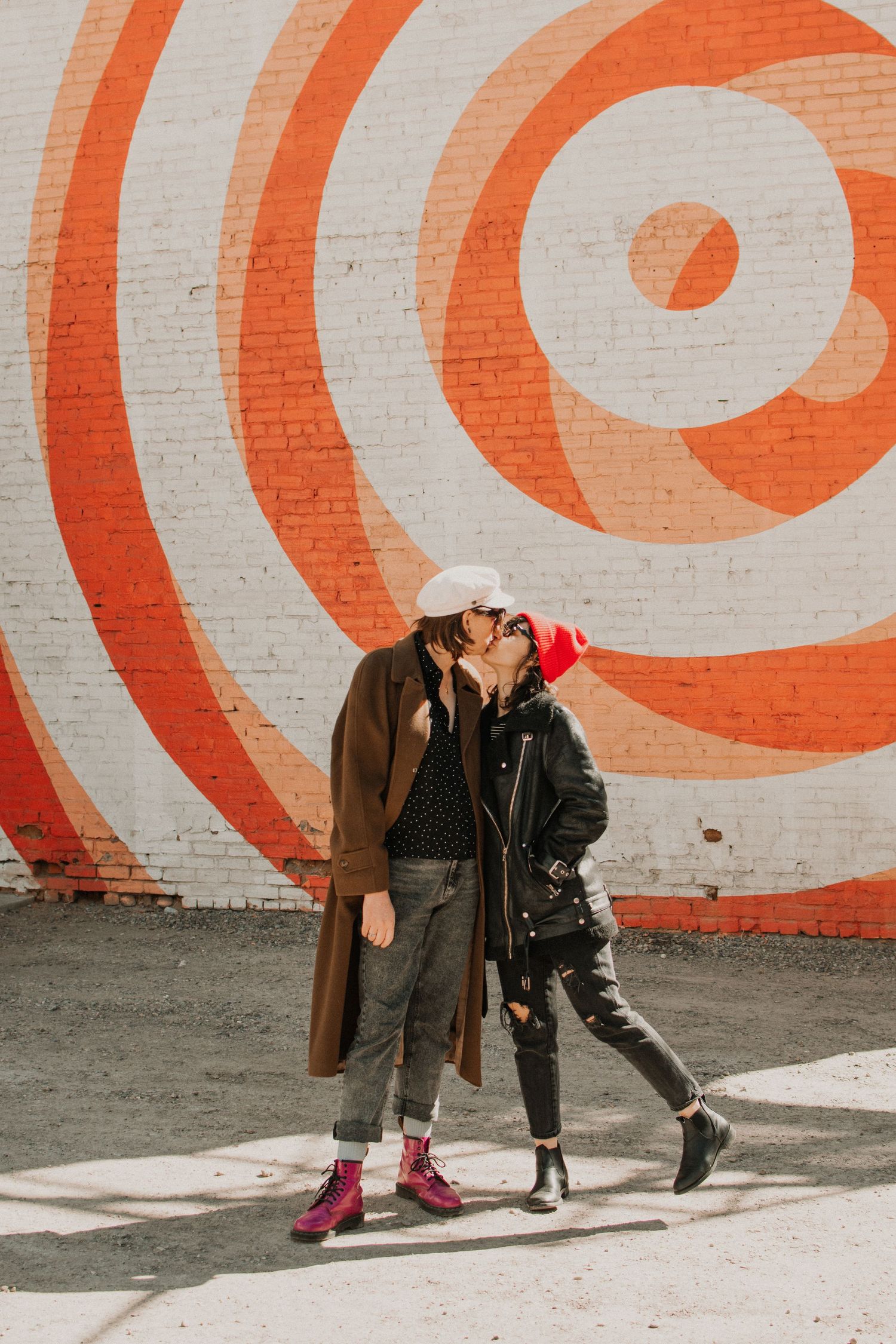Two people share an intimate moment against a wall with orange and white circular target design.
