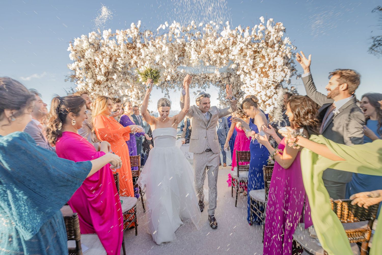 Wedding celebration with guests throwing confetti in an outdoor setting.
