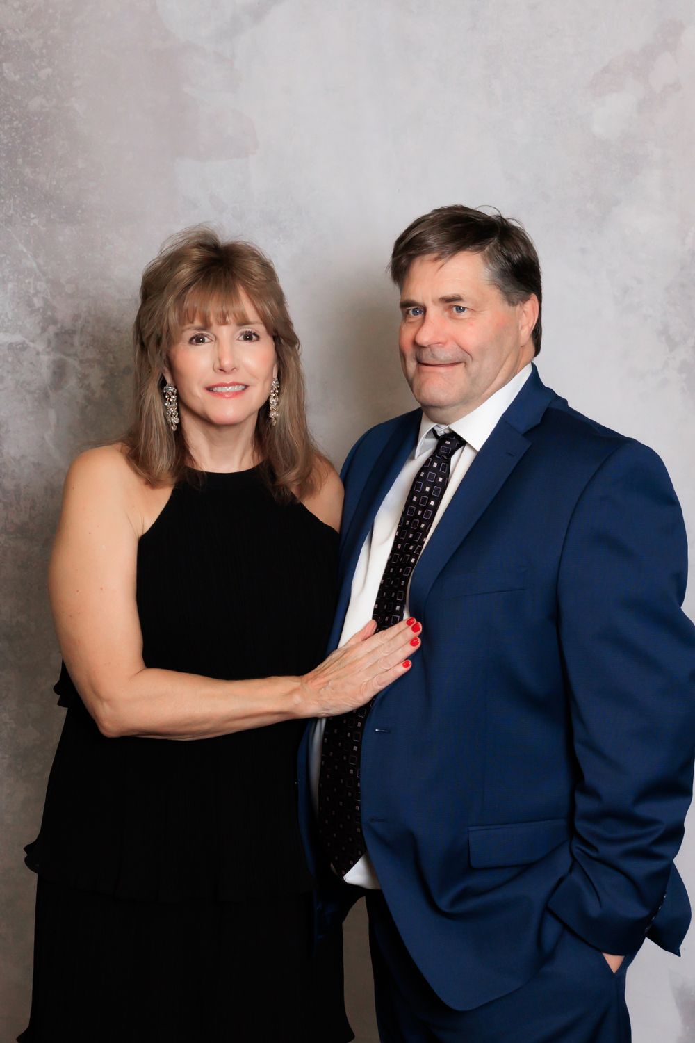 Elegant couple in formal attire posed against studio backdrop.