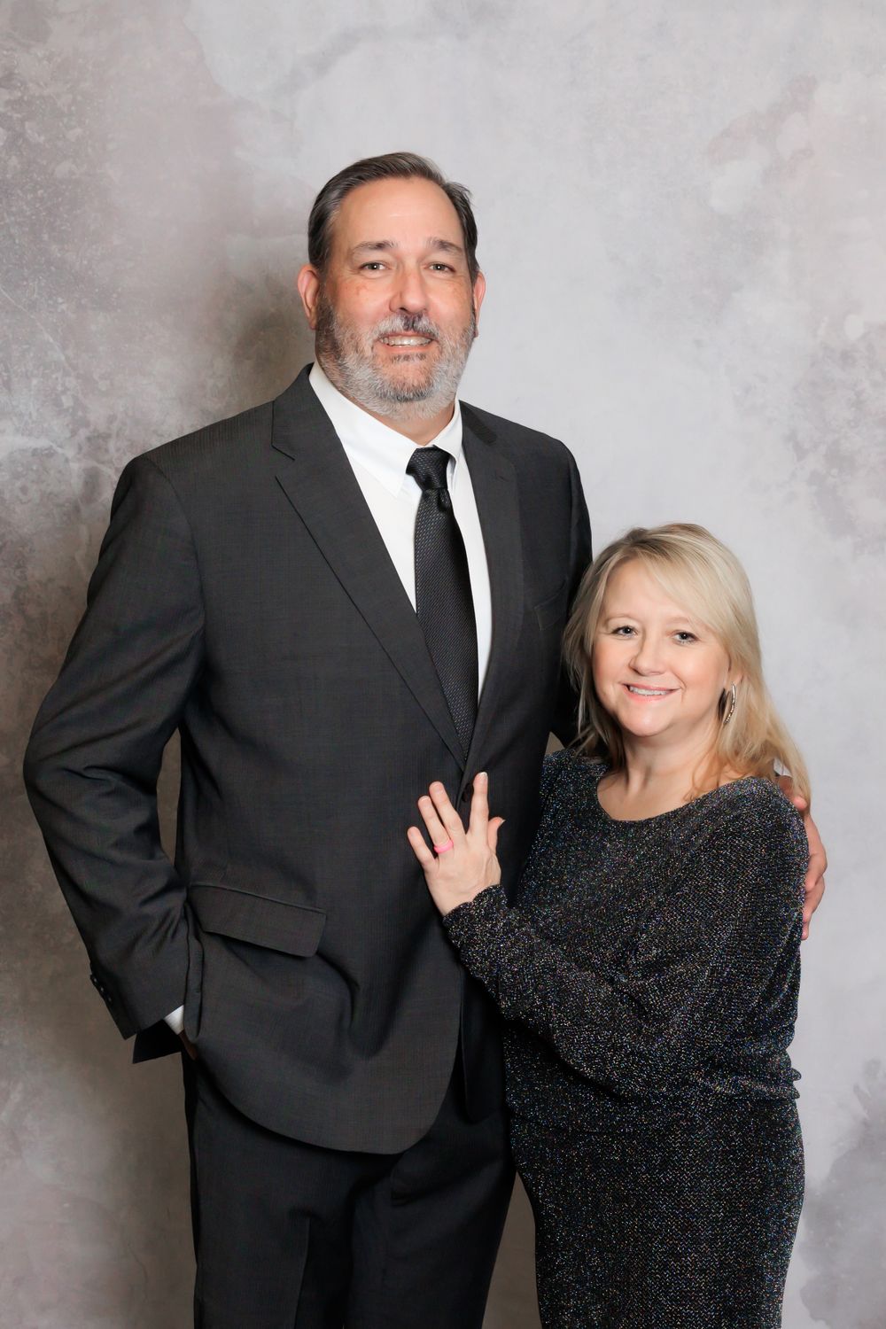 A couple in formal attire poses for a portrait, with the woman in a sparkly black top.
