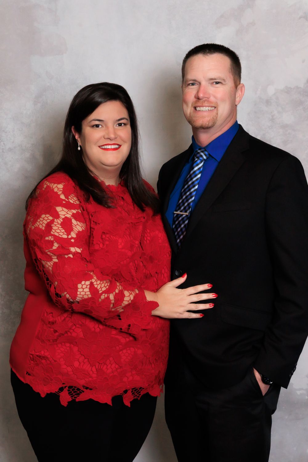 A couple poses for a portrait with the woman in red lace and man in dark suit with blue tie.