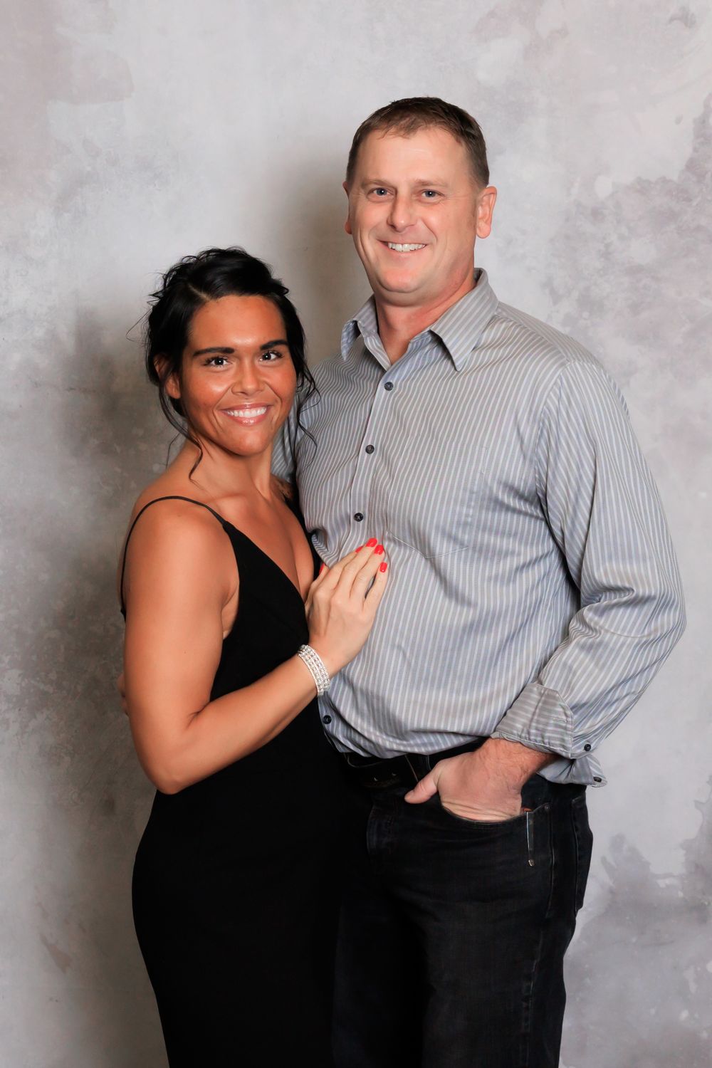 A couple poses for a portrait with woman in black dress and man in gray button-up shirt.