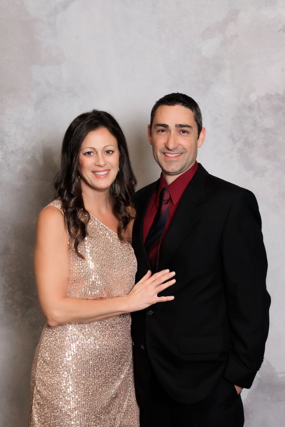 Couple poses for formal portrait with woman in sequined gold dress and man in black suit with red tie.