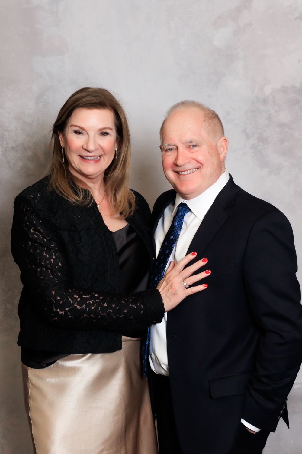 Formal portrait of couple in evening wear with woman in black lace and man in navy suit.