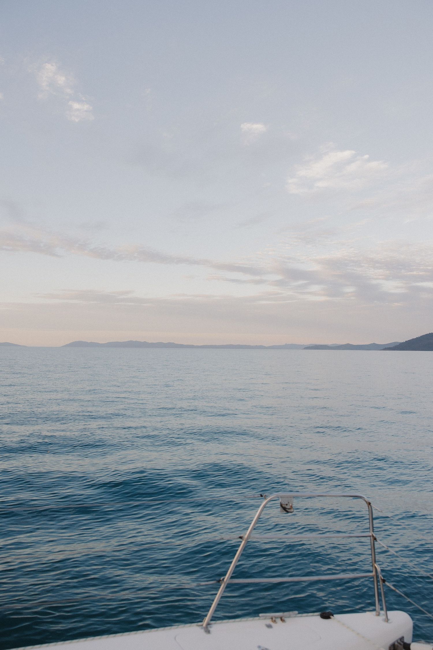 Calm blue ocean waters and distant mountains viewed from the bow of a boat.