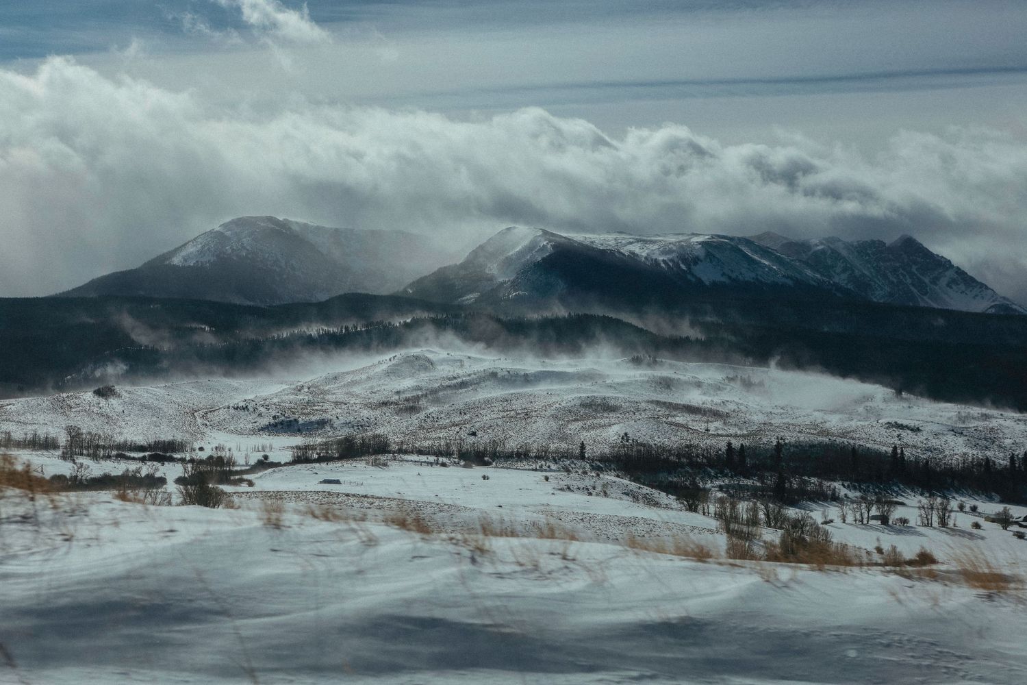 Snow-capped mountain range under cloudy winter skies with dramatic lighting.