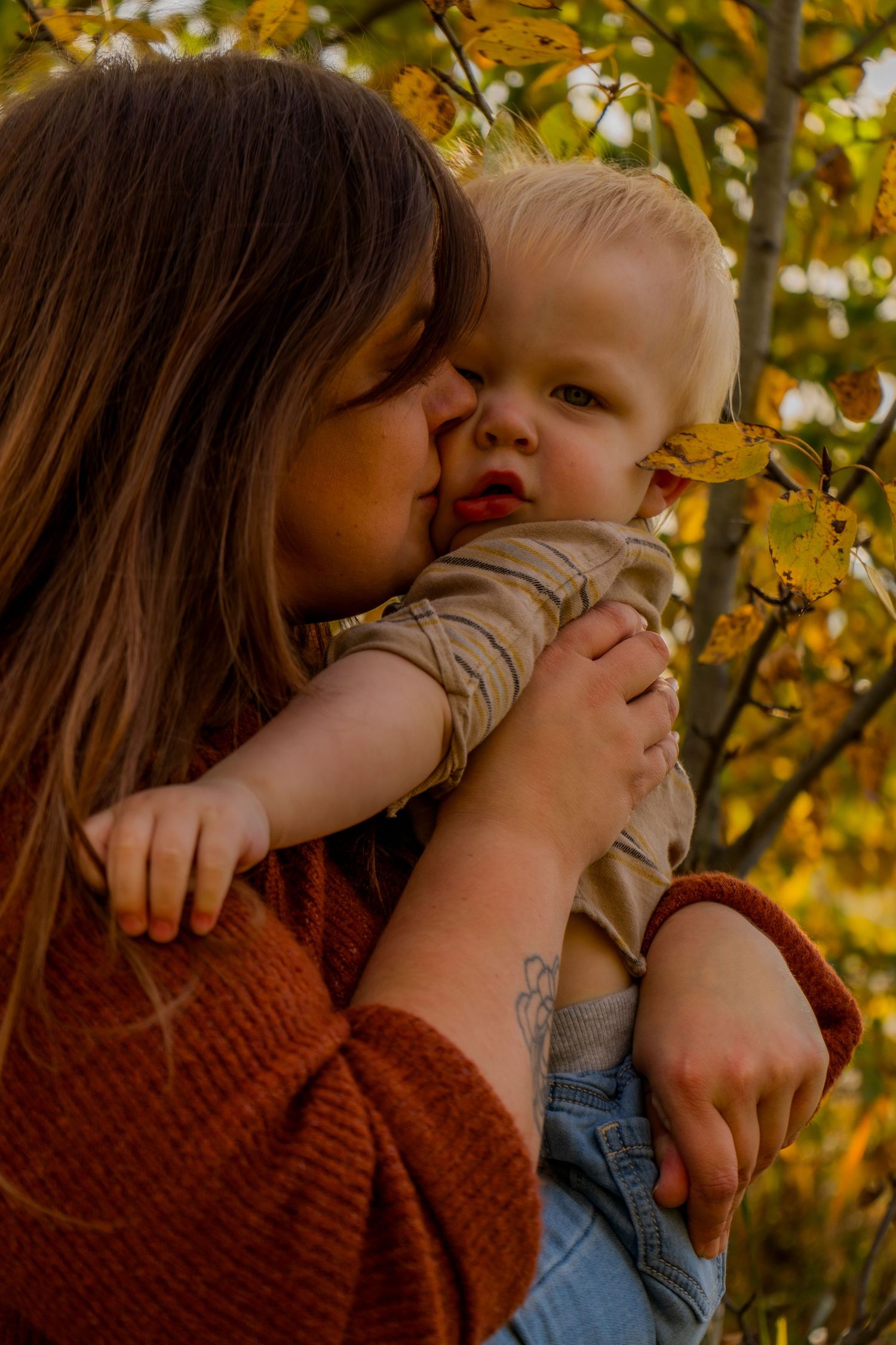 Warm autumn photography series showing tender family moments among yellow leaves.