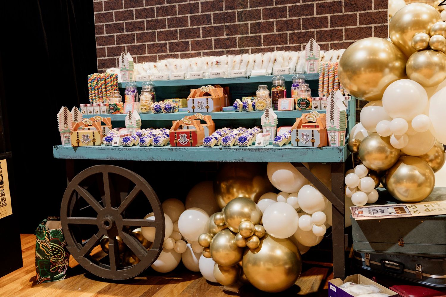 A rustic party setup with gold and white balloon garlands, wooden accents, and vintage-style decorative elements.