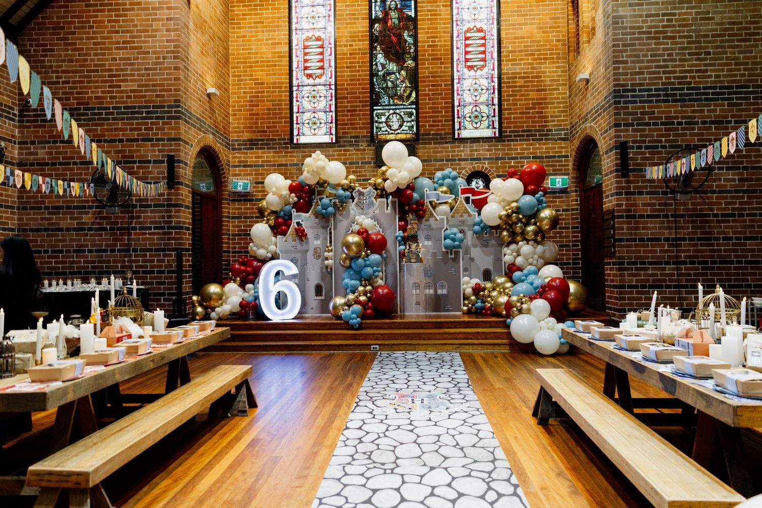 Rustic wedding reception setup in historic brick venue with long wooden tables and red and white balloon decorations.