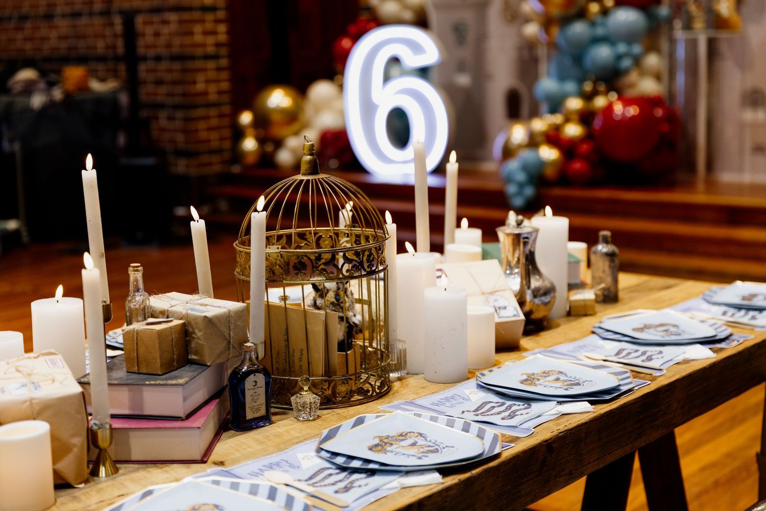 Elegant table setting with white candles, blue plates, and gold accents on a wooden surface in a rustic setting.