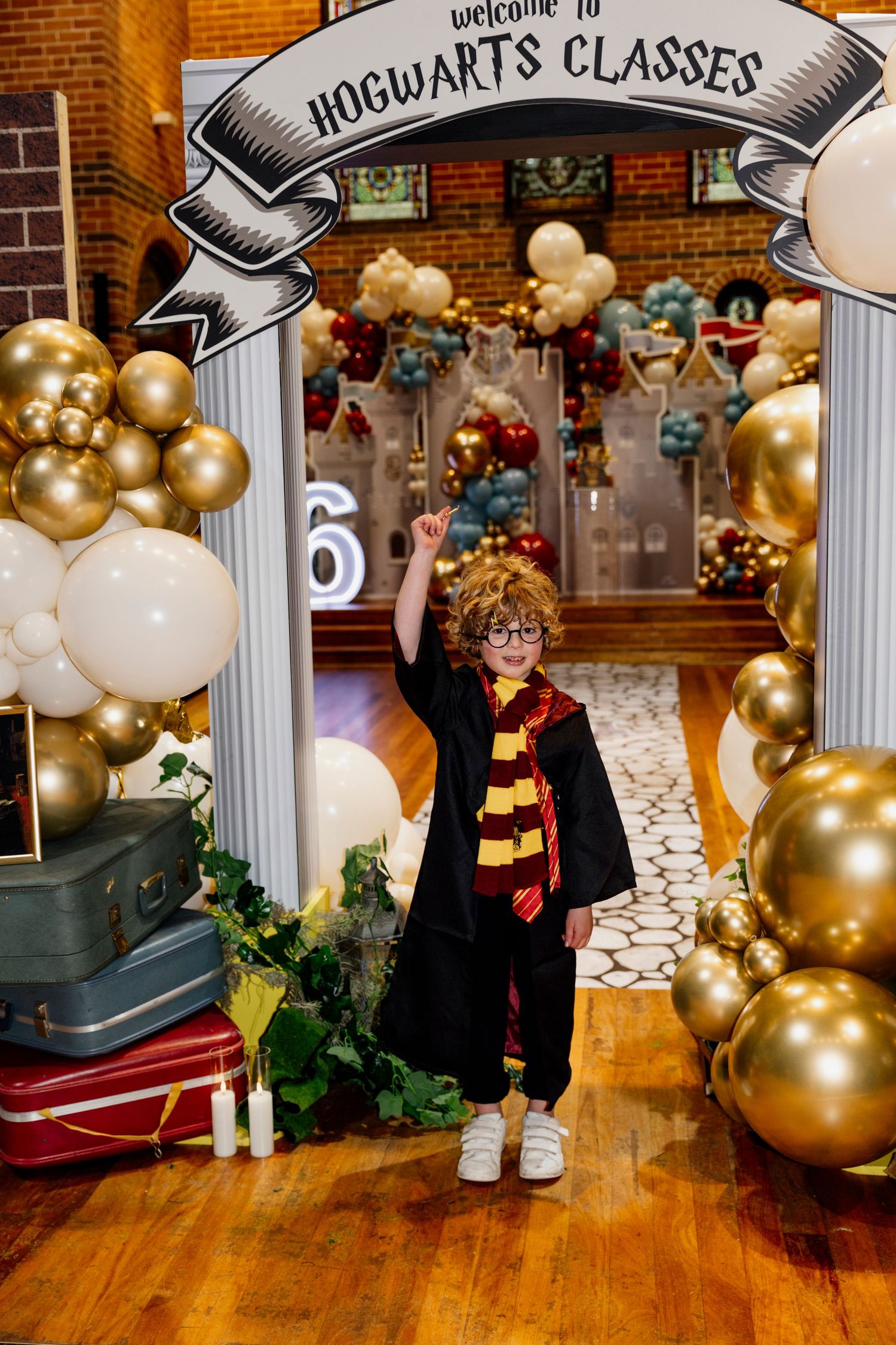 Harry Potter themed party decor with gold balloons, columns, and brick wall backdrop creates magical atmosphere.