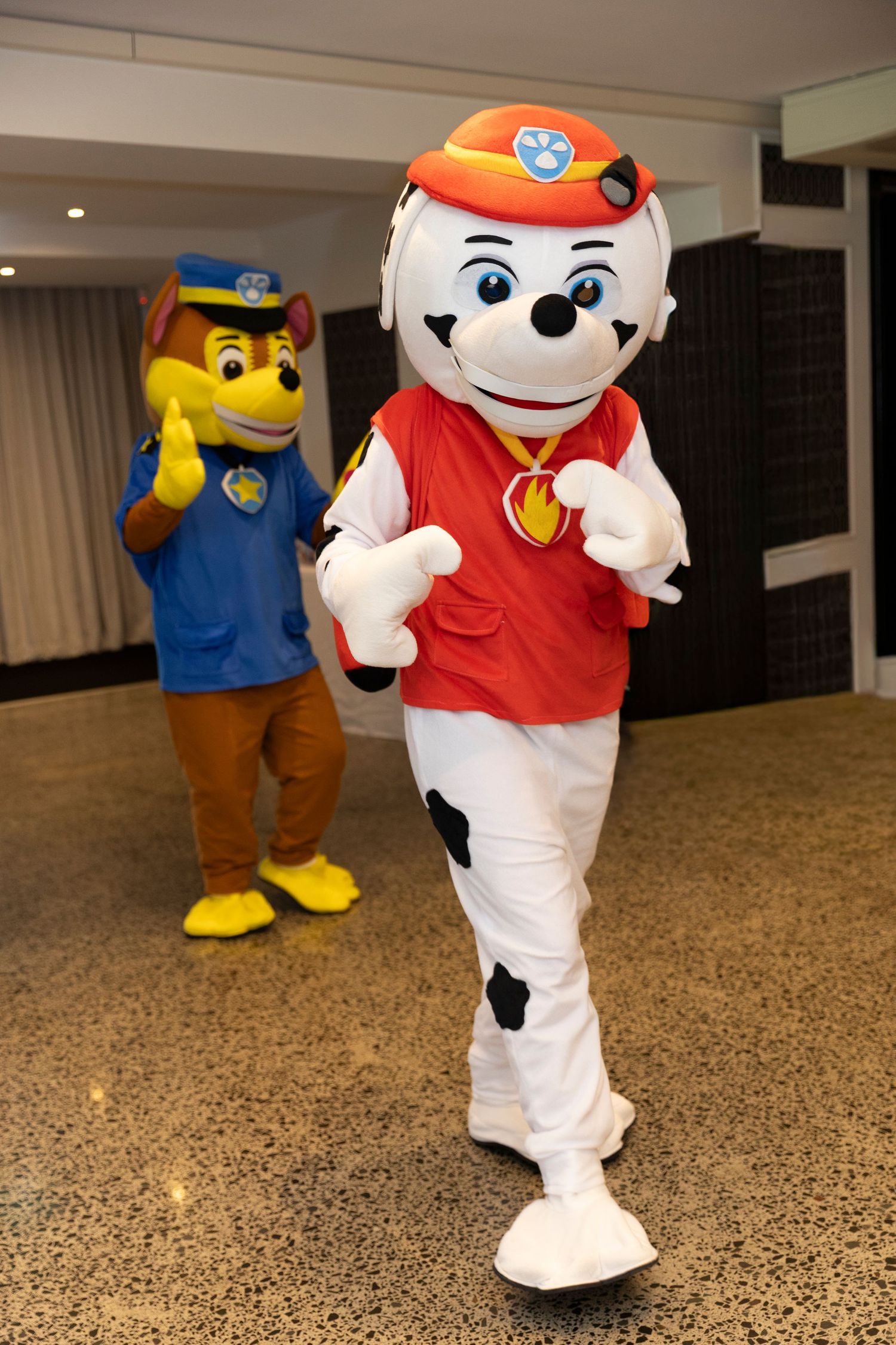 Costumed mascot characters in blue and red outfits dancing and posing in a carpeted indoor space.