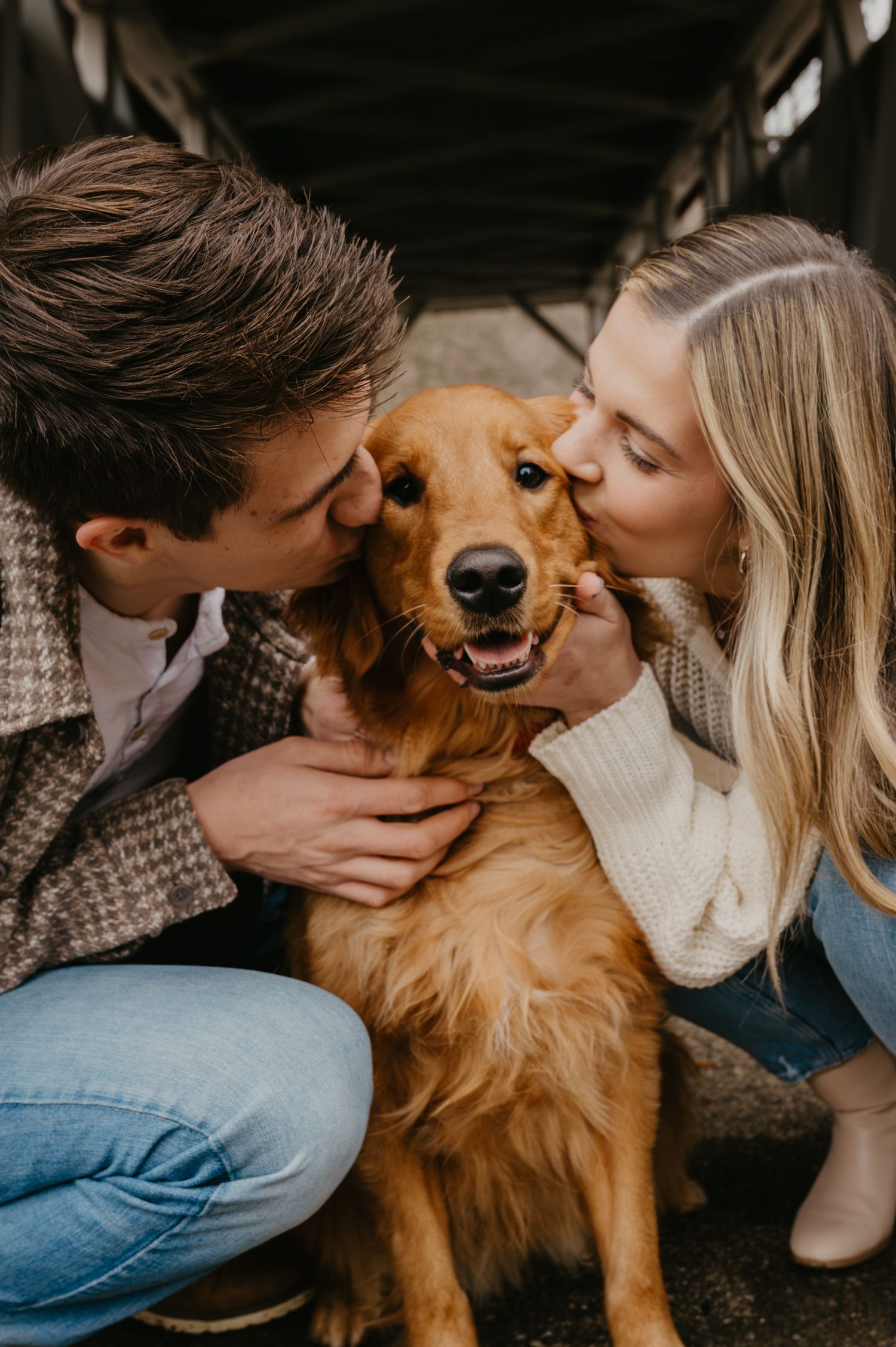 Young couple kissing their happy golden retriever dog on both cheeks.