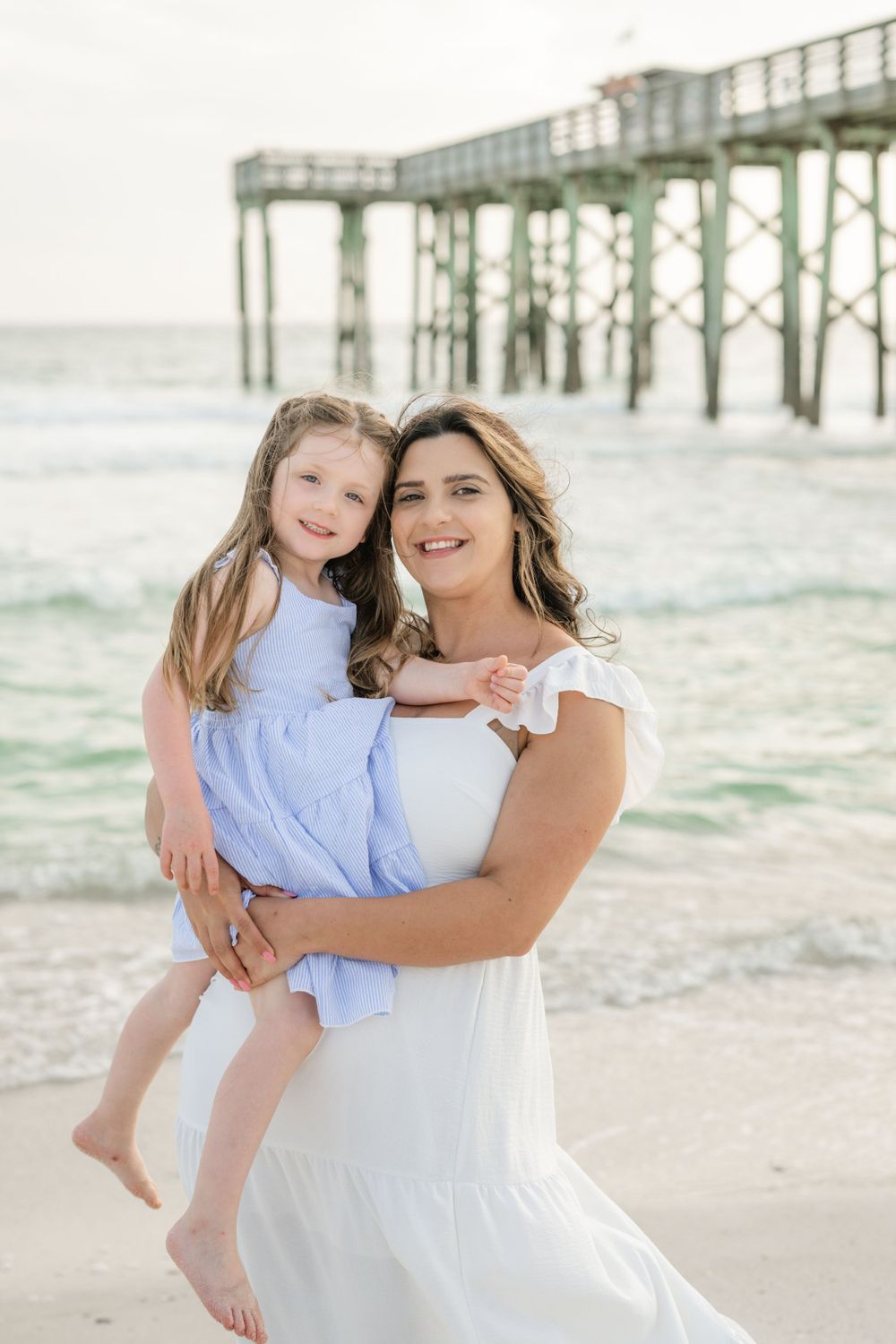 A tender beach portrait in white and blue outfits by a wooden pier.