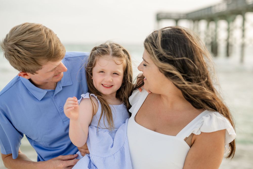 Intimate family moment captured during a beach photoshoot near a wooden pier.