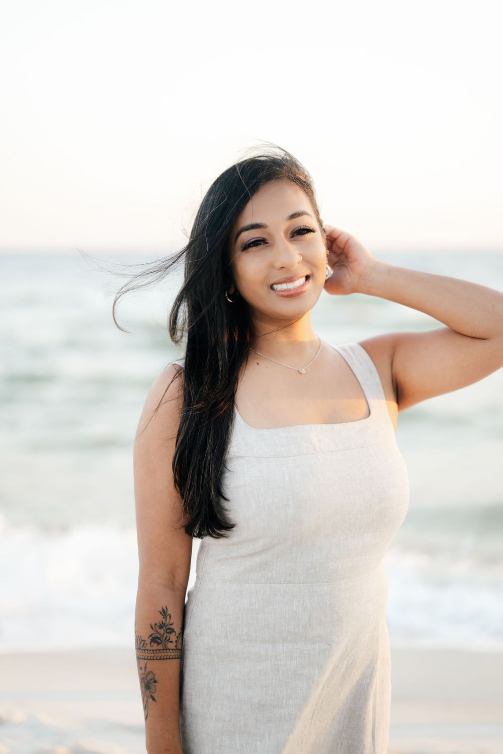 Woman in white dress smiles while posing on beach at sunset.