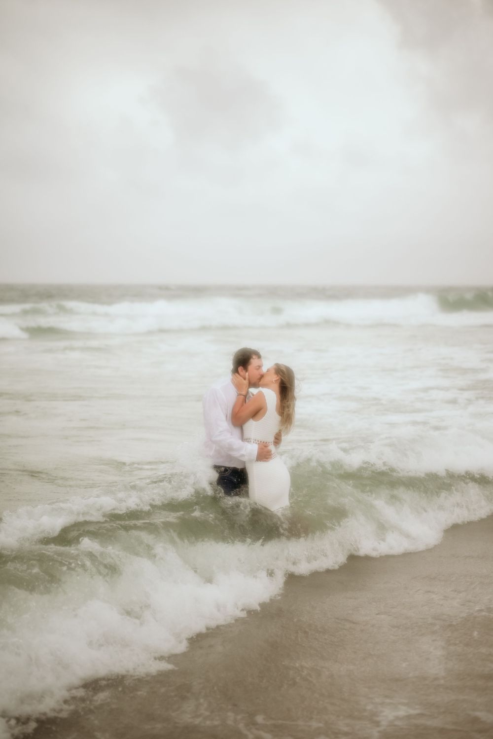 Dreamy beach engagement photo of couple embracing in ocean waves.