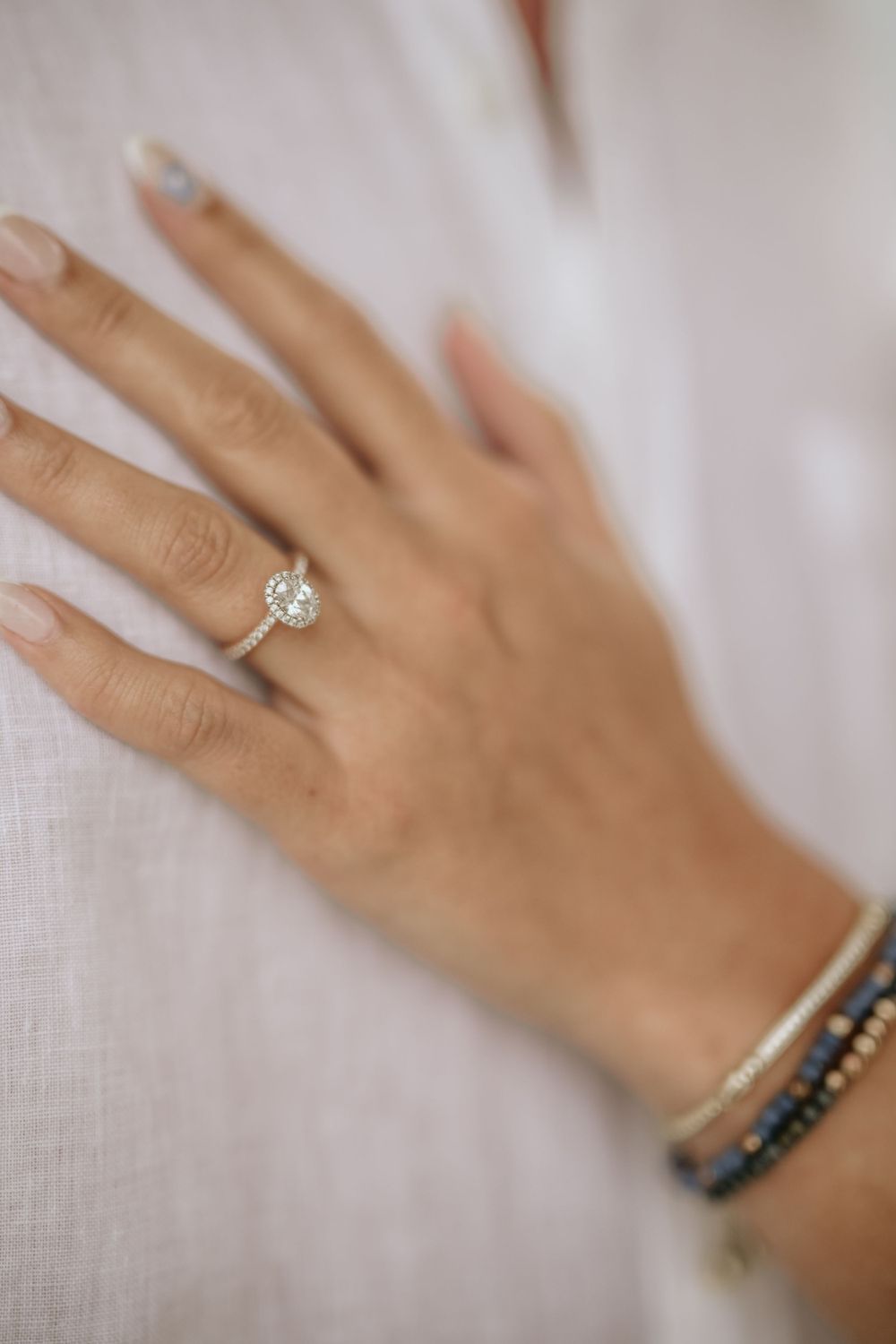 Close-up of a hand wearing an elegant diamond engagement ring and delicate bracelet against a white background.