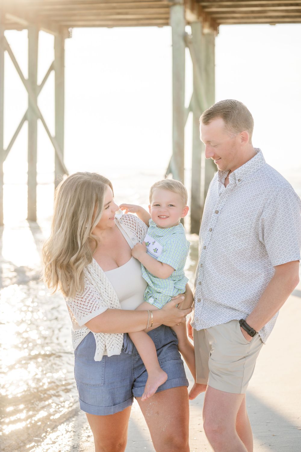 A family shares a tender moment together under a beach pier.