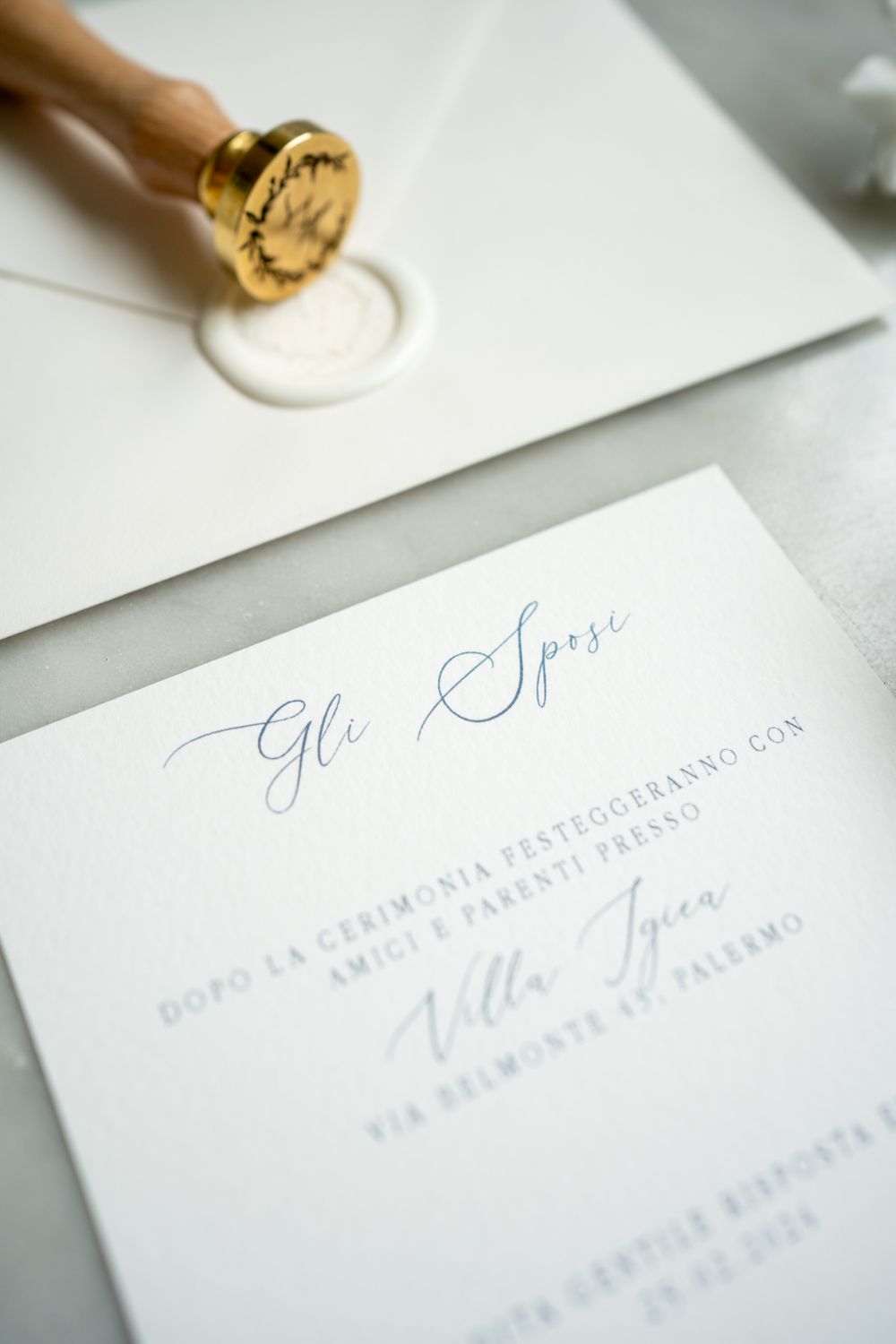Calligraphy wedding invitation being stamped with wax seal on white paper.