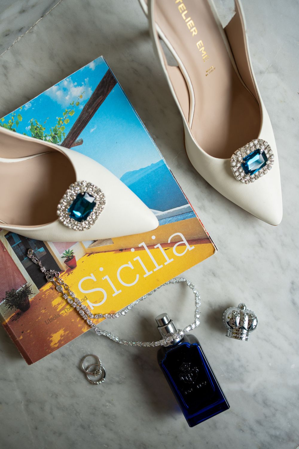 White bridal shoes with crystal embellishments alongside Sicily travel postcards and jewelry.