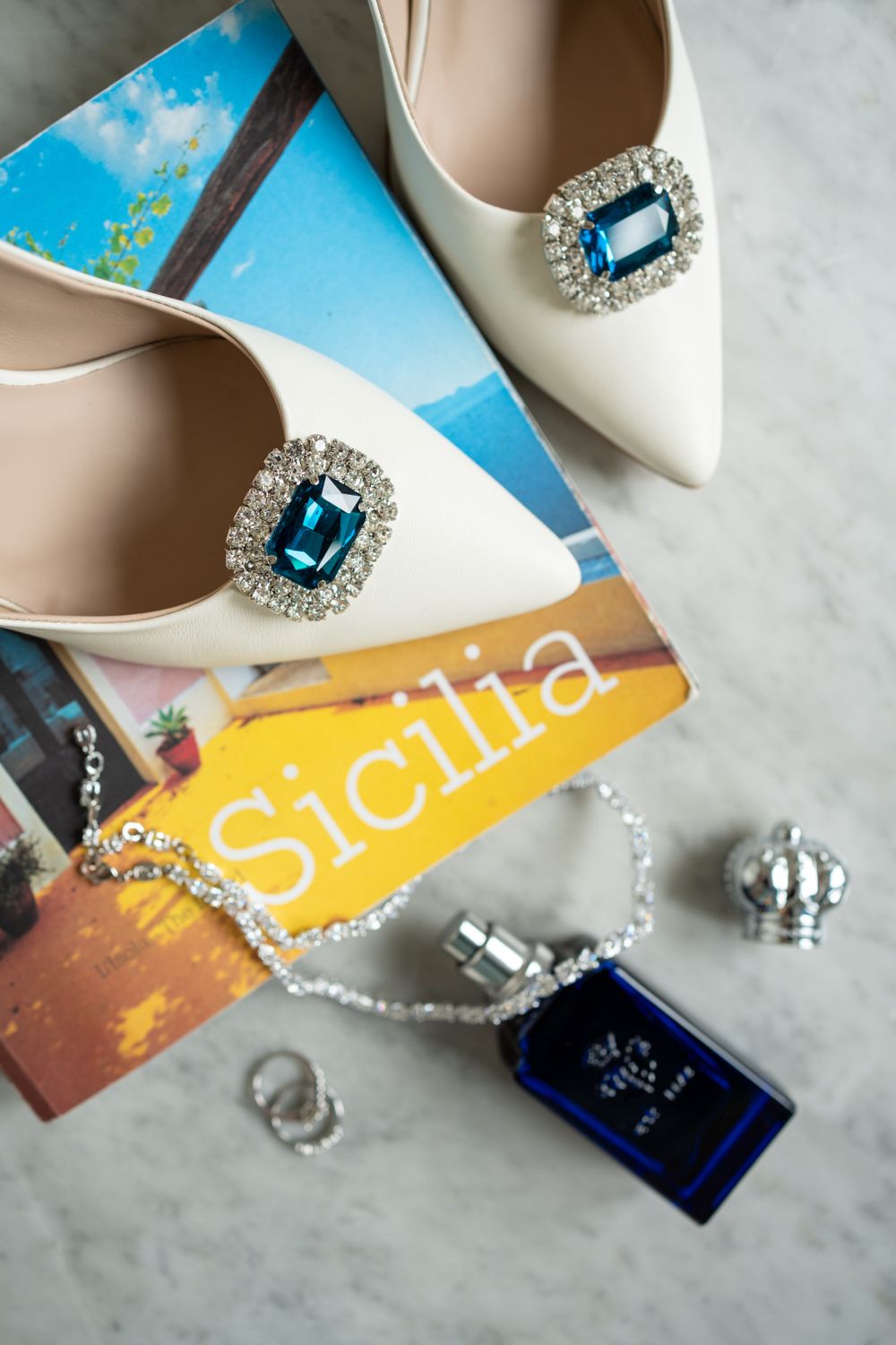 Elegant white wedding shoes with blue crystal details displayed with Sicily travel postcards.