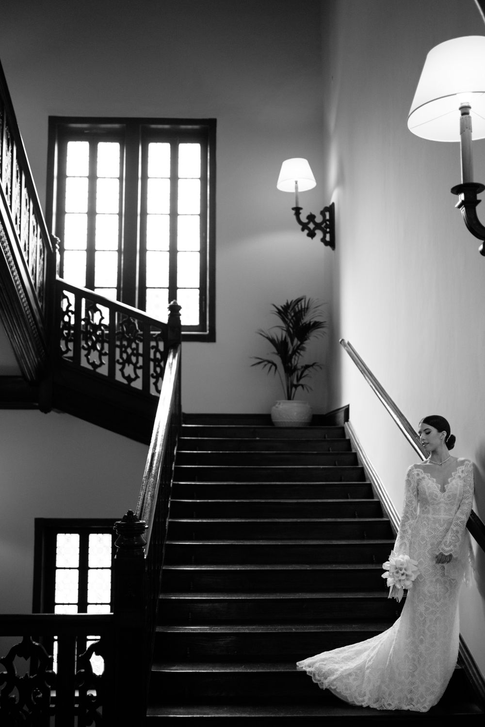 Moody black and white composition of bride in lace gown on vintage staircase.