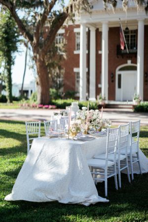 Elegant outdoor wedding table setup with white linens and chiavari chairs against a Southern mansion with white columns.