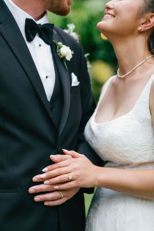 Close-up of newlyweds showing wedding rings, bow tie, and white boutonniere.