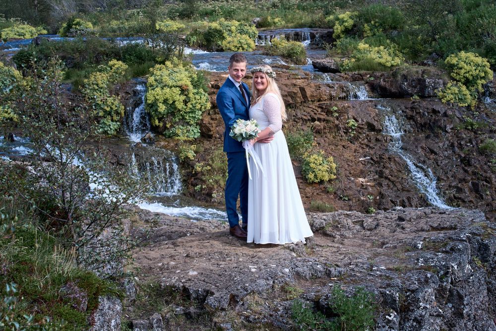A wedding portrait against a scenic background of cascading waterfalls and lush greenery.
