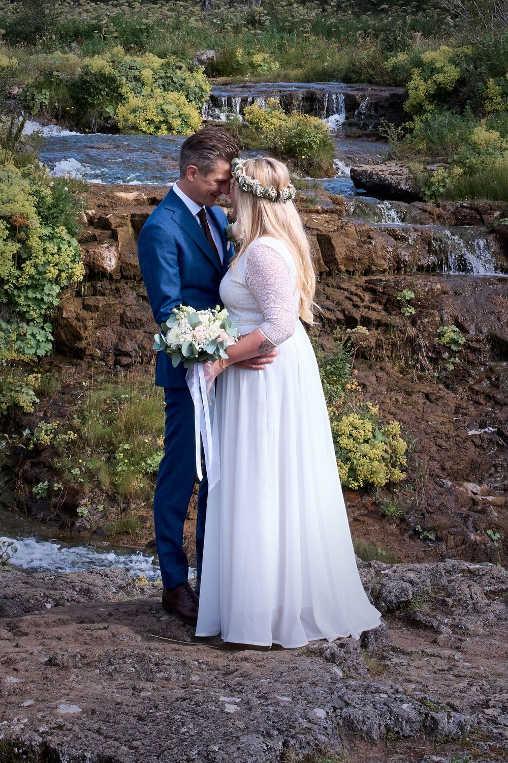 A newlywed couple shares an intimate moment in front of cascading waterfalls.