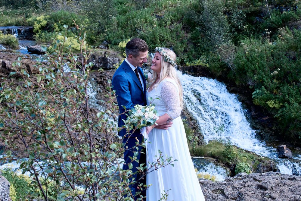 A couple celebrates their wedding day beside a rushing waterfall in natural surroundings.