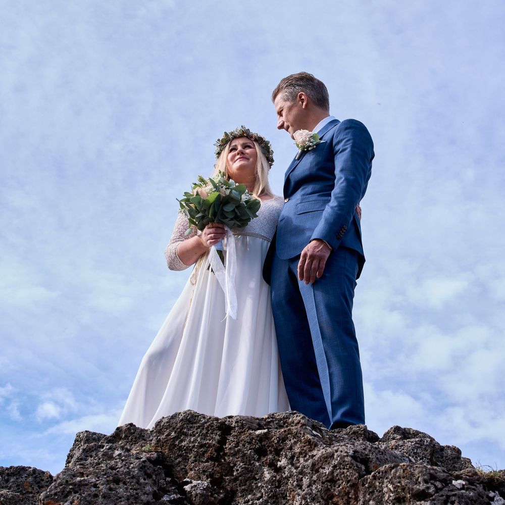 A wedding couple stands atop a rocky outcrop against a blue sky backdrop.
