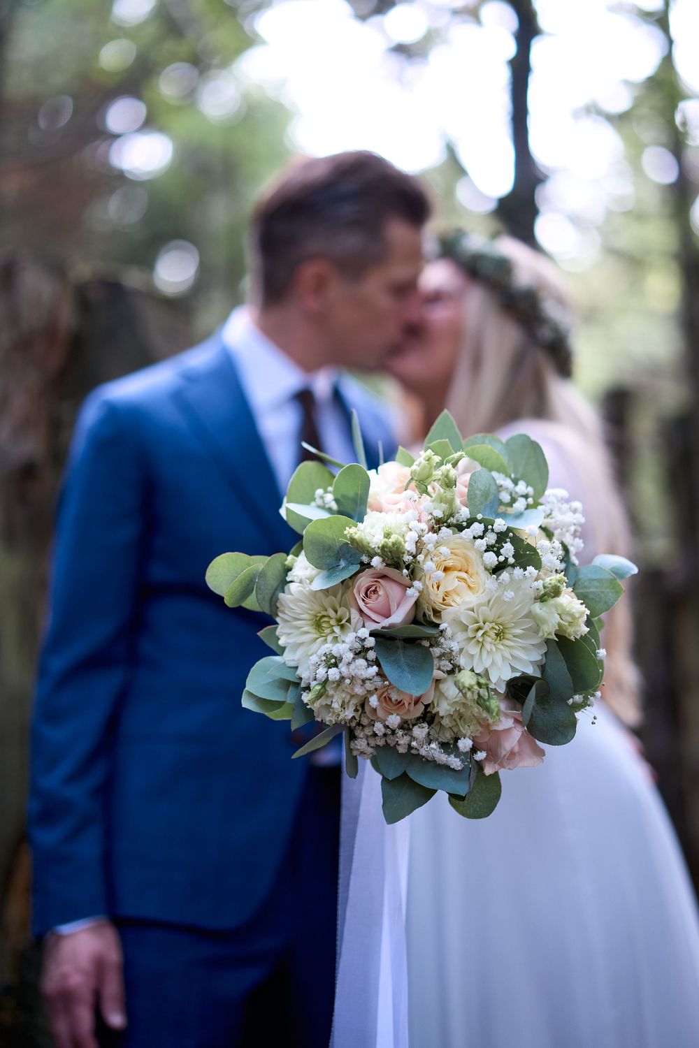 Elegant wedding bouquet with roses and eucalyptus leaves in focus with couple in background.