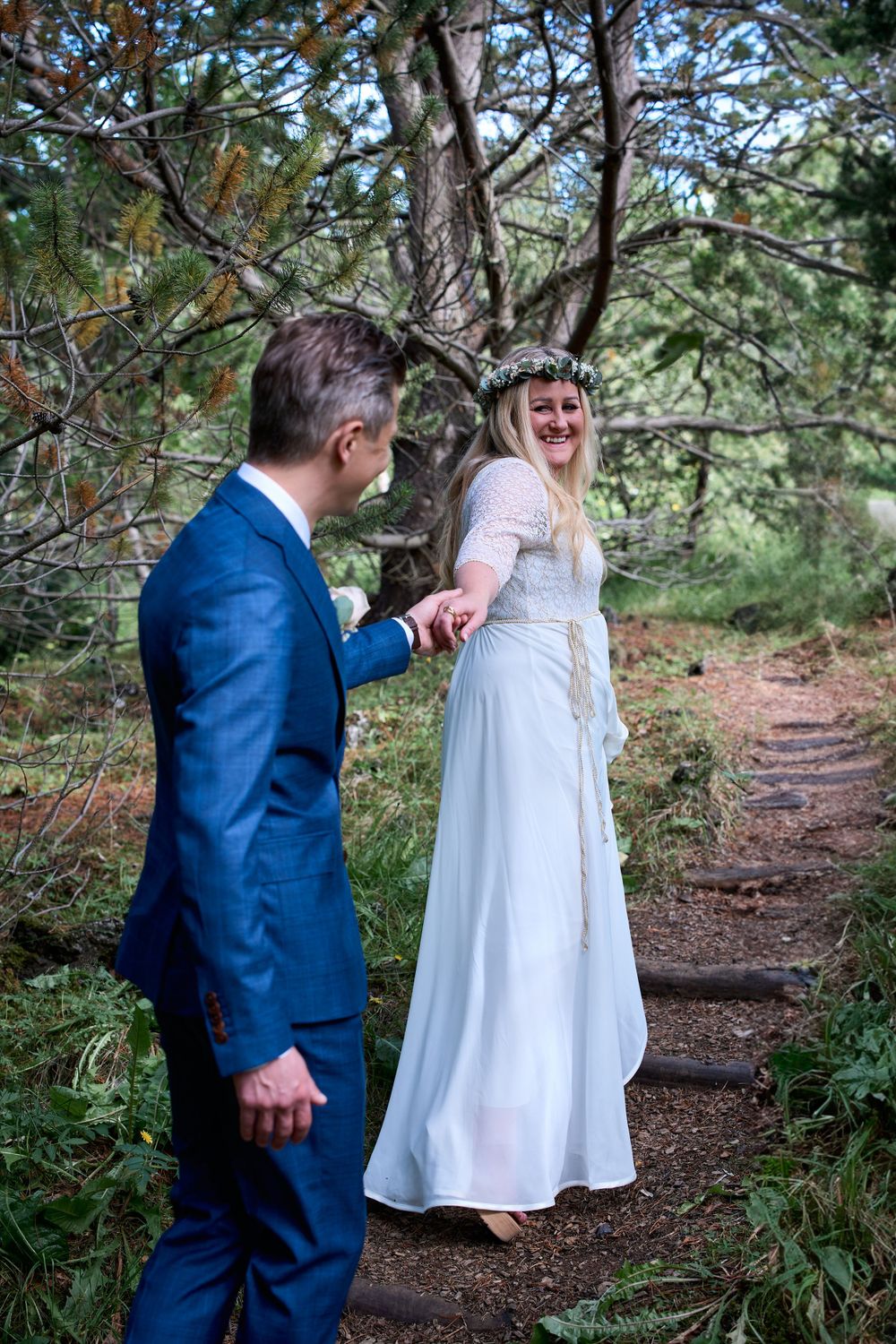 A joyful wedding moment captured on a forest path with pine trees.