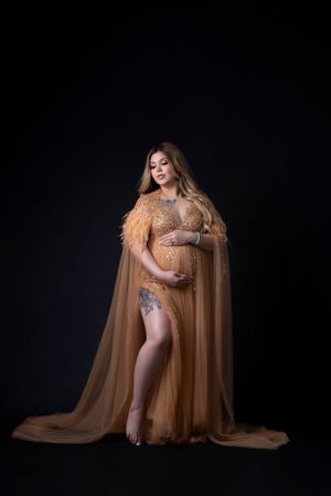 Elegant maternity session with champagne-colored tulle gown in low-key lighting.