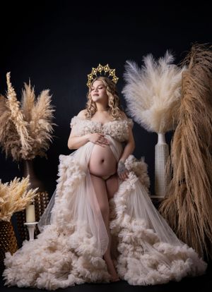 A dreamy maternity portrait with pampas grass decor and a flowing cream-colored gown with gold crown.