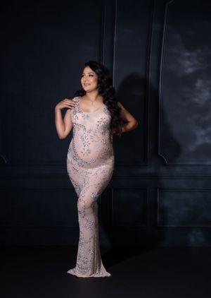 Elegant maternity portraits in sparkly pink gown against dark wall.